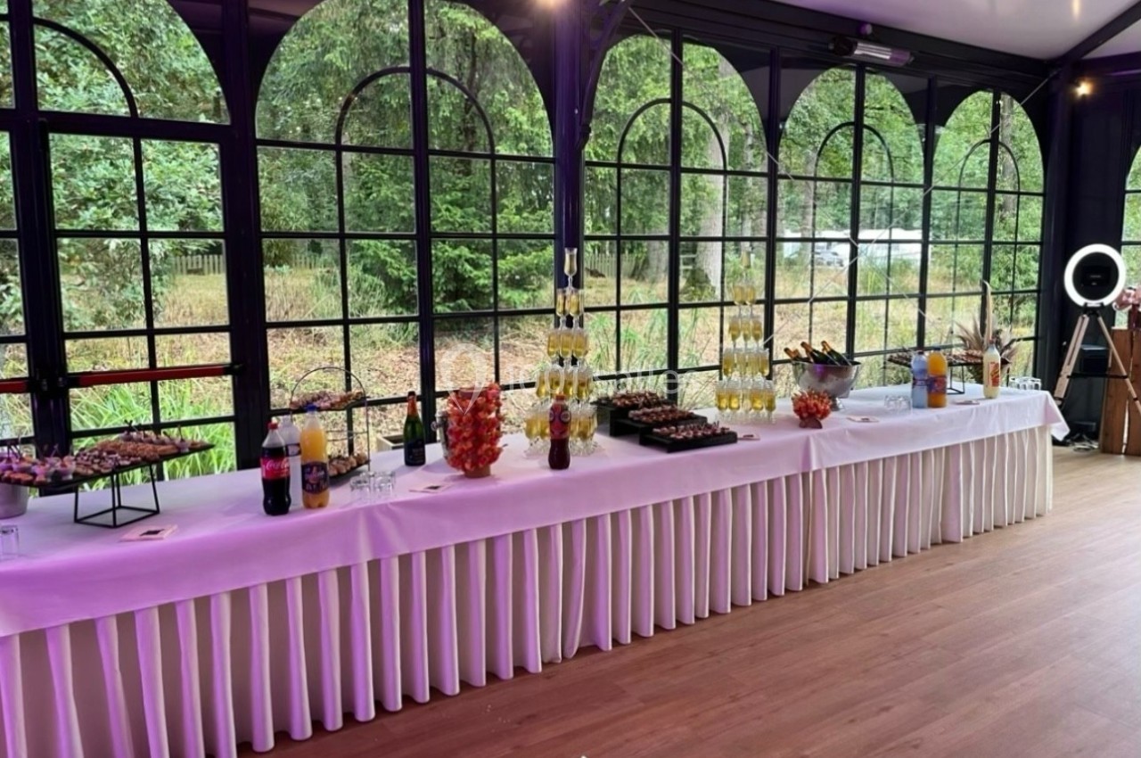 Table de buffet dressée avec boissons, verrines, fruits et desserts, dans une salle lumineuse avec vue sur un jardin.