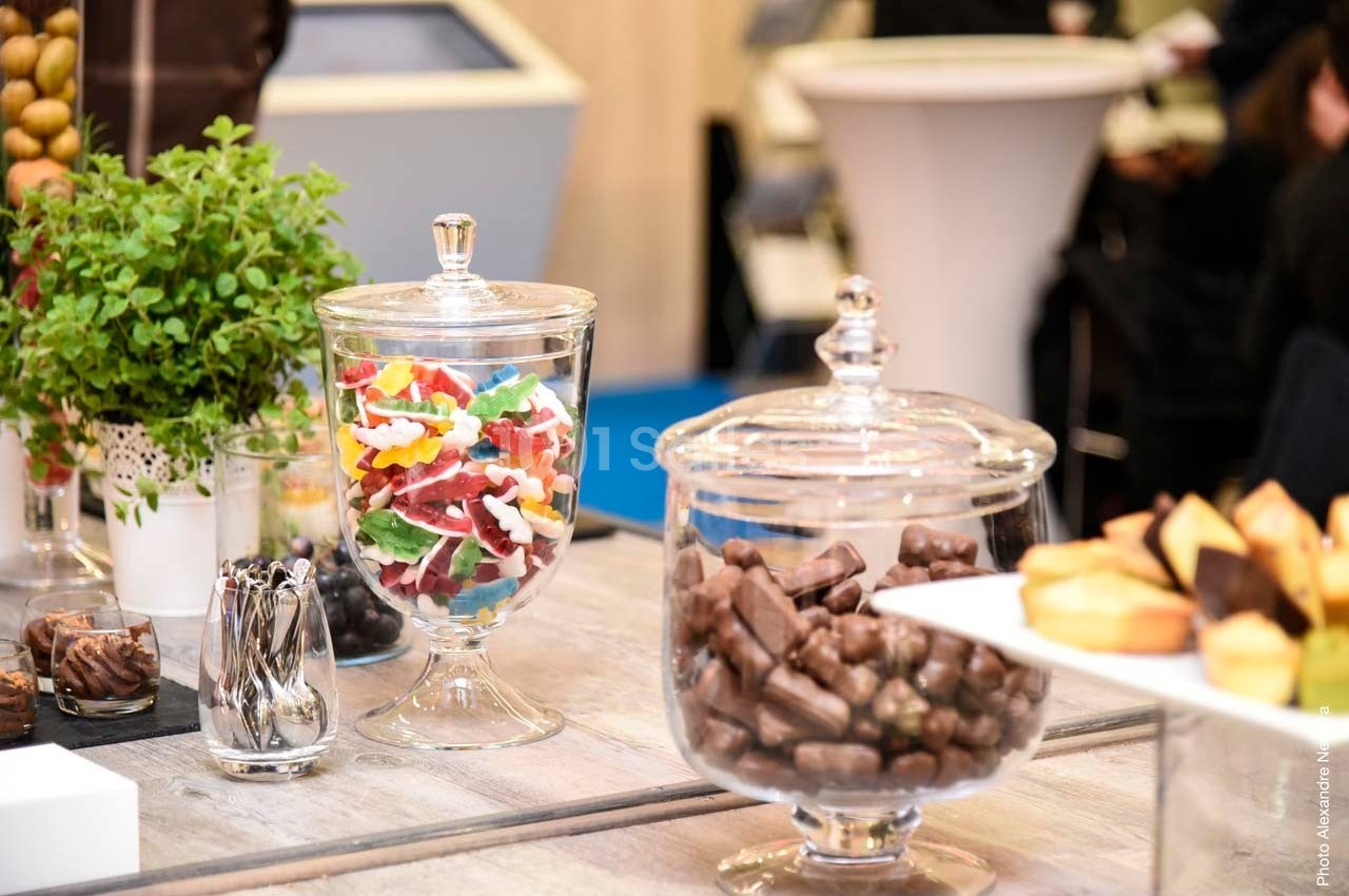 Des bonbons colorés, des chocolats et des pâtisseries sont disposés dans des bonbonnières sur une table en bois.