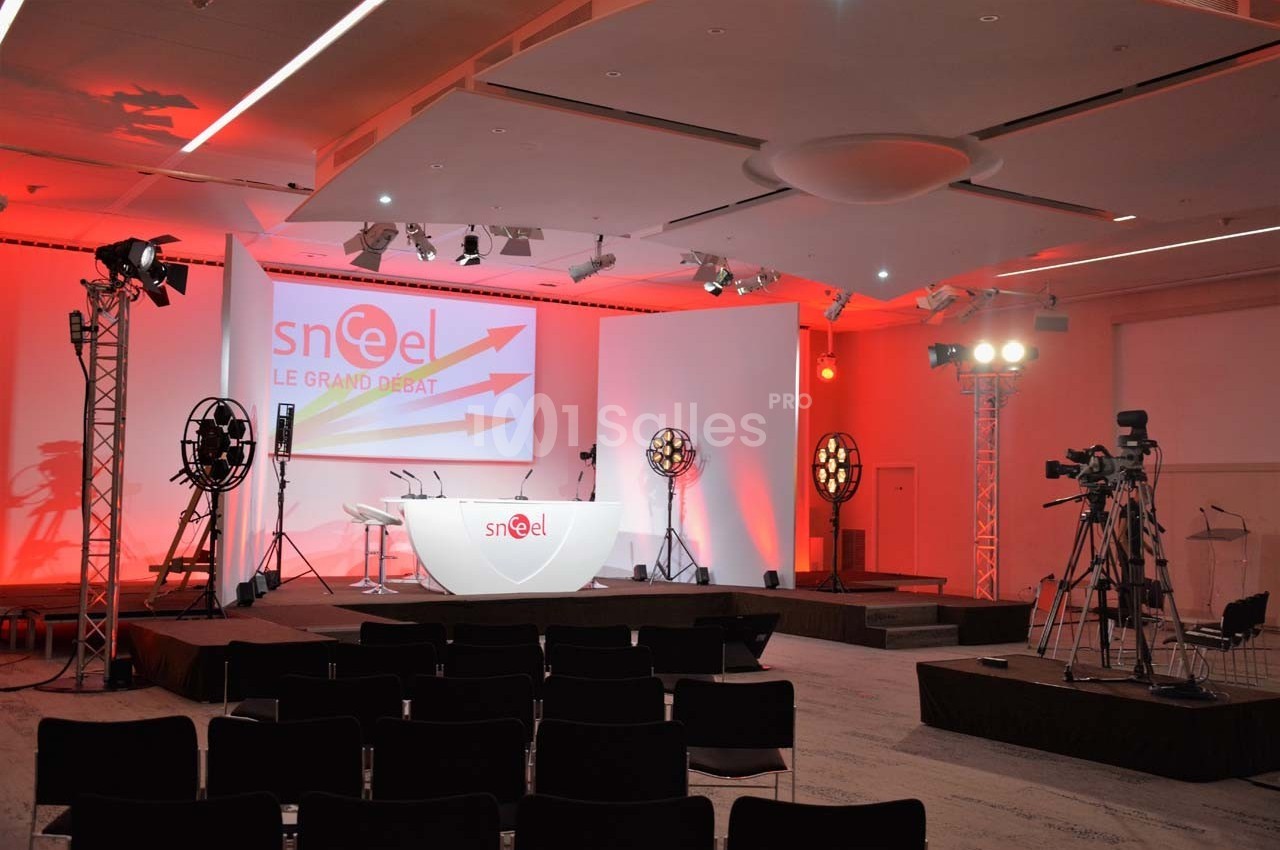 Salle de conférence équipée de projecteurs, caméras et écran de projection avec un pupitre sur scène.