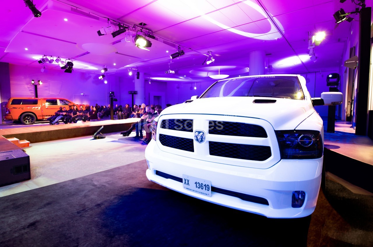 Un pick-up blanc exposé dans une salle éclairée de lumières violettes, avec un public en arrière-plan.