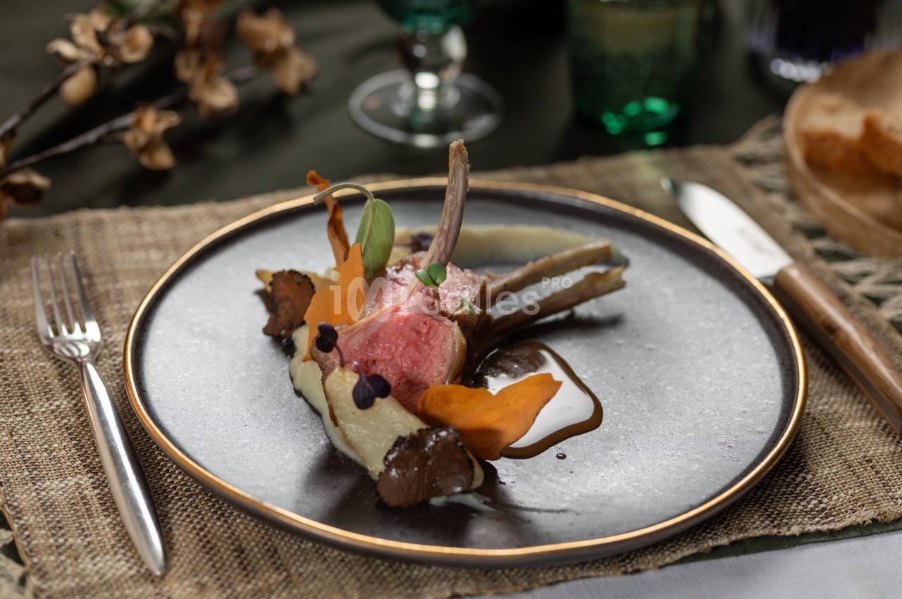Carré d'agneau rôti avec purée, légumes racines et sauce, présenté sur une assiette élégante.