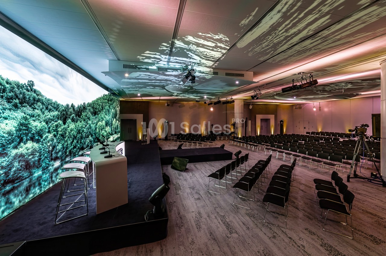 Salle de conférence moderne avec écrans panoramiques affichant une forêt et des rangées de sièges disposées en face.