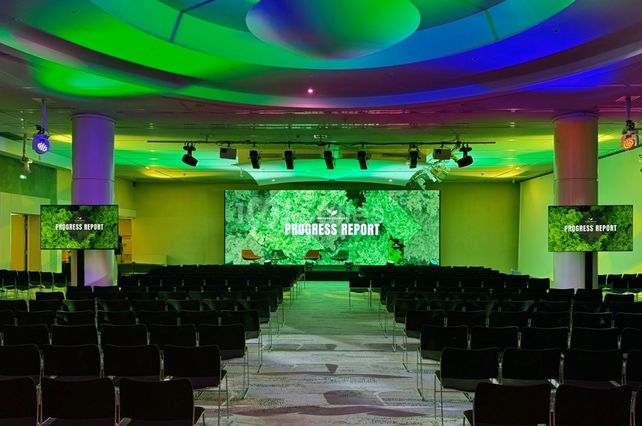 Salle de conférence vide avec des écrans affichant ’Progress Report’ et un éclairage vert et bleu.