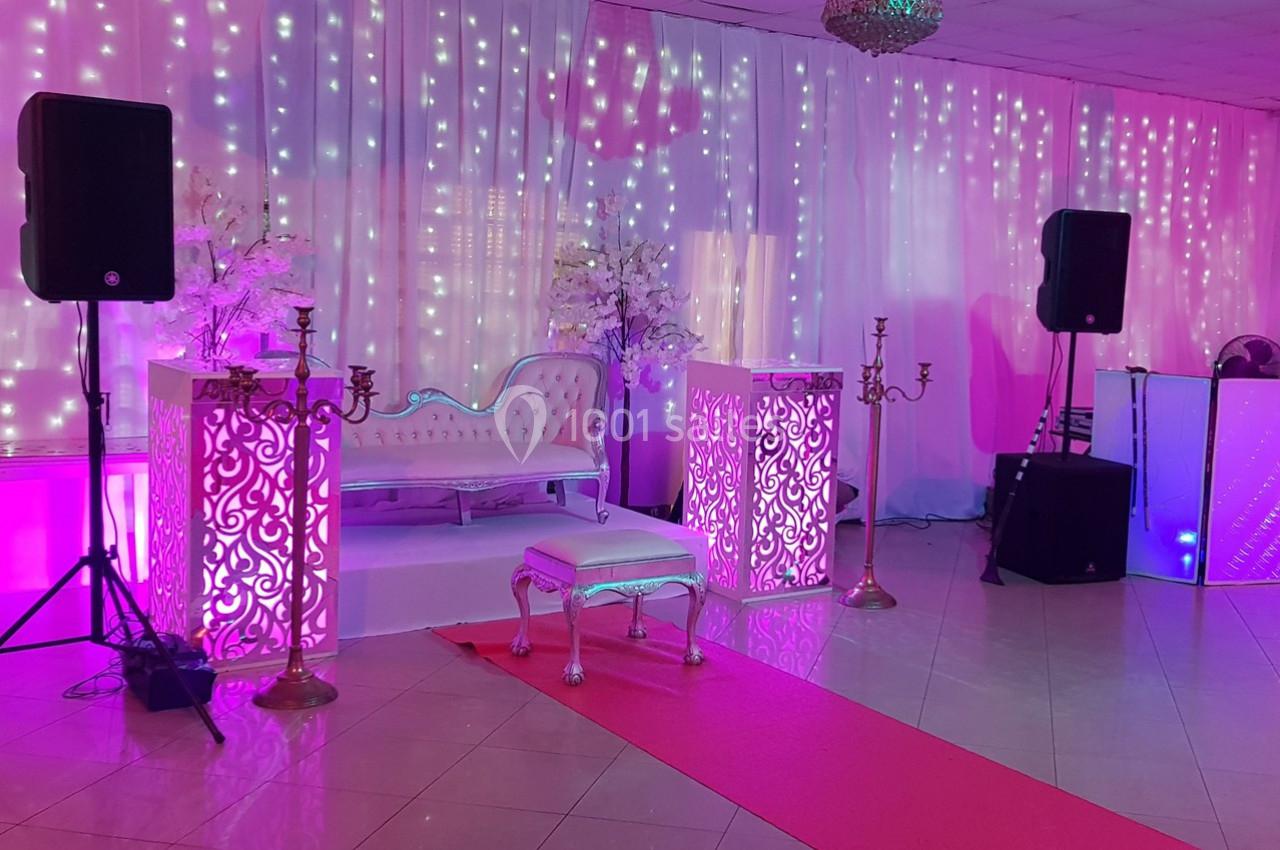 Salle décorée pour un événement avec canapé blanc, éclairages roses et guirlandes lumineuses en arrière-plan.