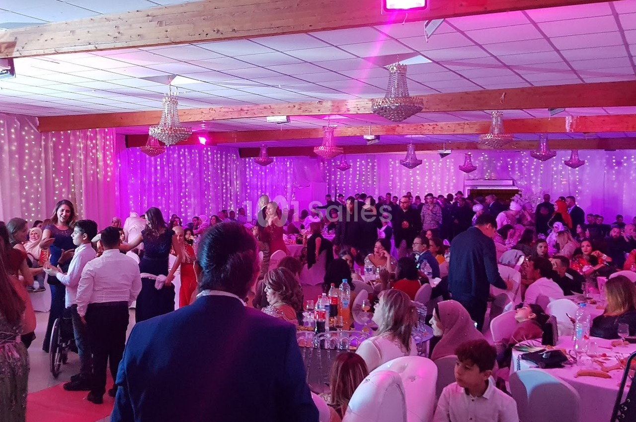 Salle de réception animée avec de nombreuses personnes assises ou debout, éclairée par des lumières roses et décorée de…