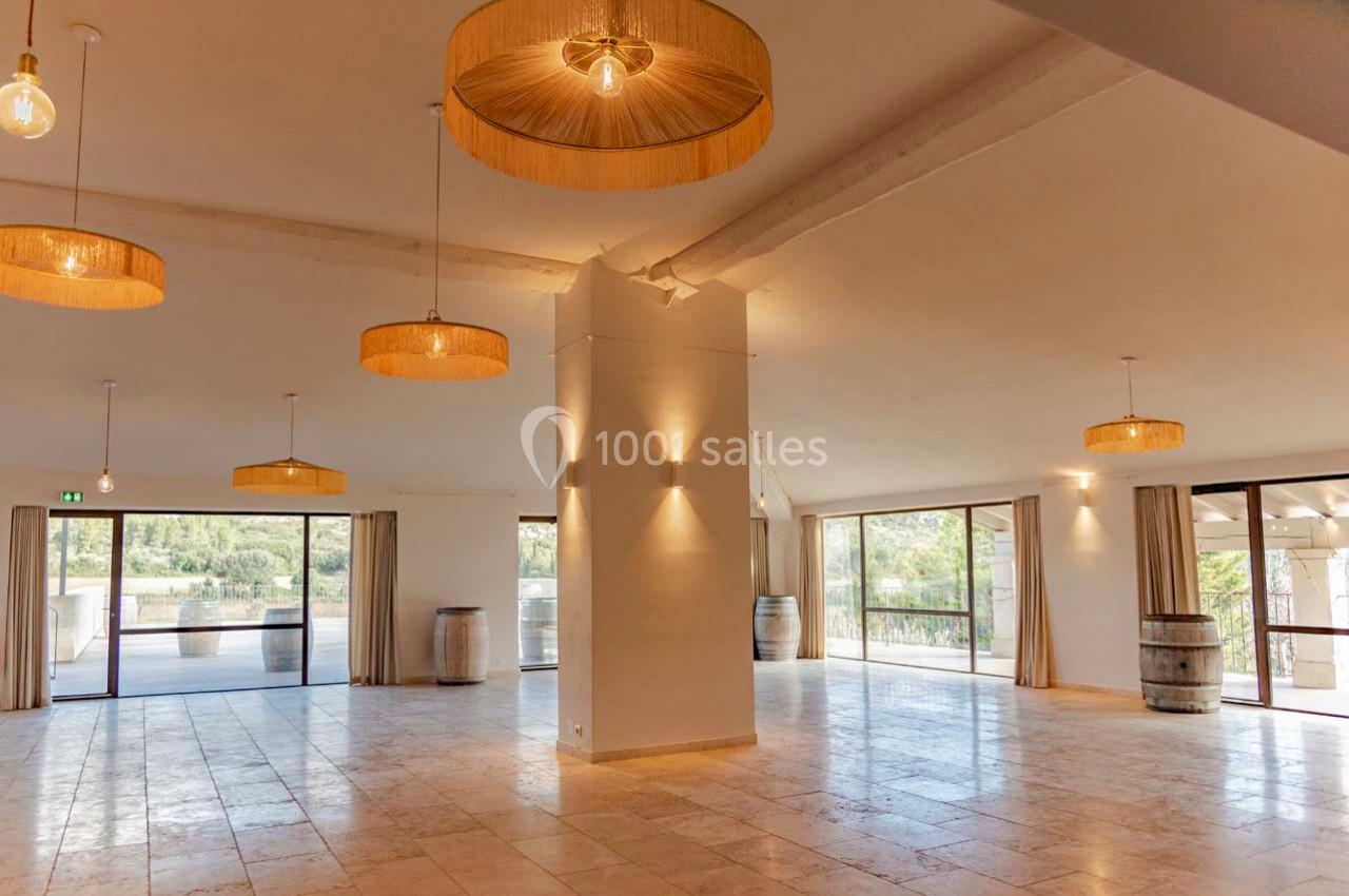 Salle lumineuse avec grandes baies vitrées, sol en carrelage clair, suspensions en osier et tonneaux en décoration.