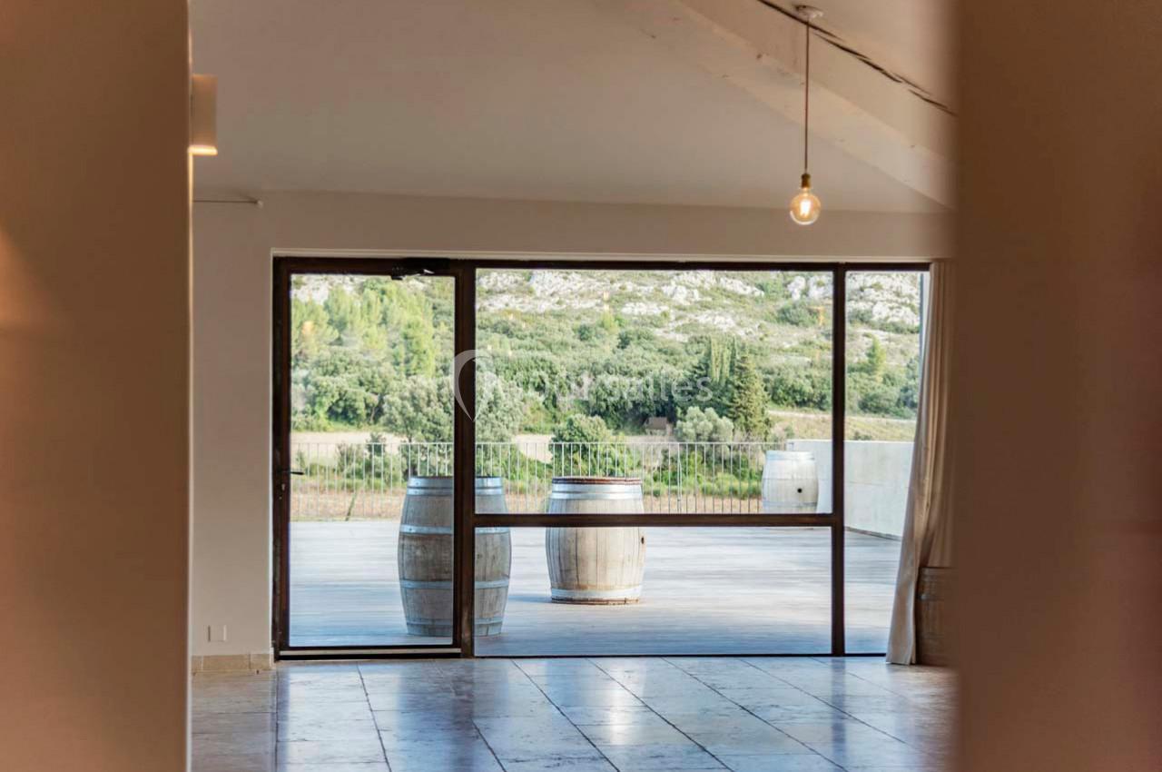 Vue sur une terrasse avec deux tonneaux en bois, encadrée par une grande baie vitrée donnant sur un paysage naturel.