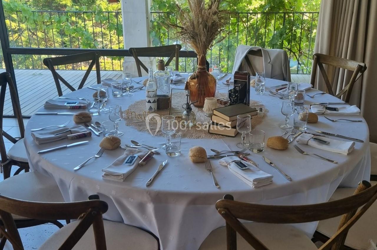 Table ronde dressée pour un repas, décorée avec des livres, un bouquet de fleurs séchées et des couverts disposés.