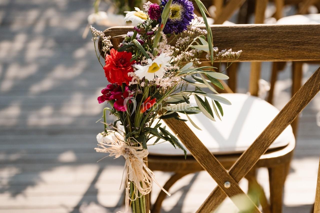 Chaises en bois décorées de bouquets de fleurs colorées, alignées sur une terrasse ensoleillée.
