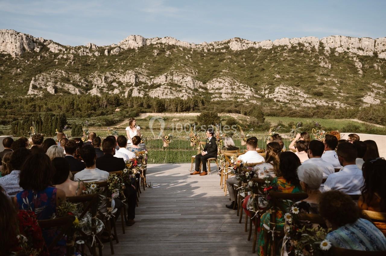 Cérémonie de mariage en plein air avec des invités assis, vue sur des montagnes et une végétation verdoyante en arrière-plan.