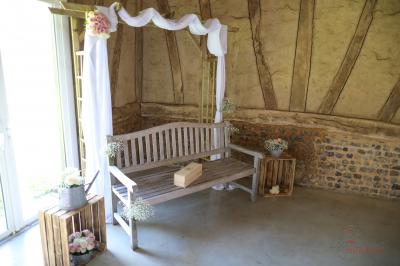 Banc en bois sous une arche décorée de feuilles d'automne, entouré de bougies et de feuilles au sol dans une salle rustique.