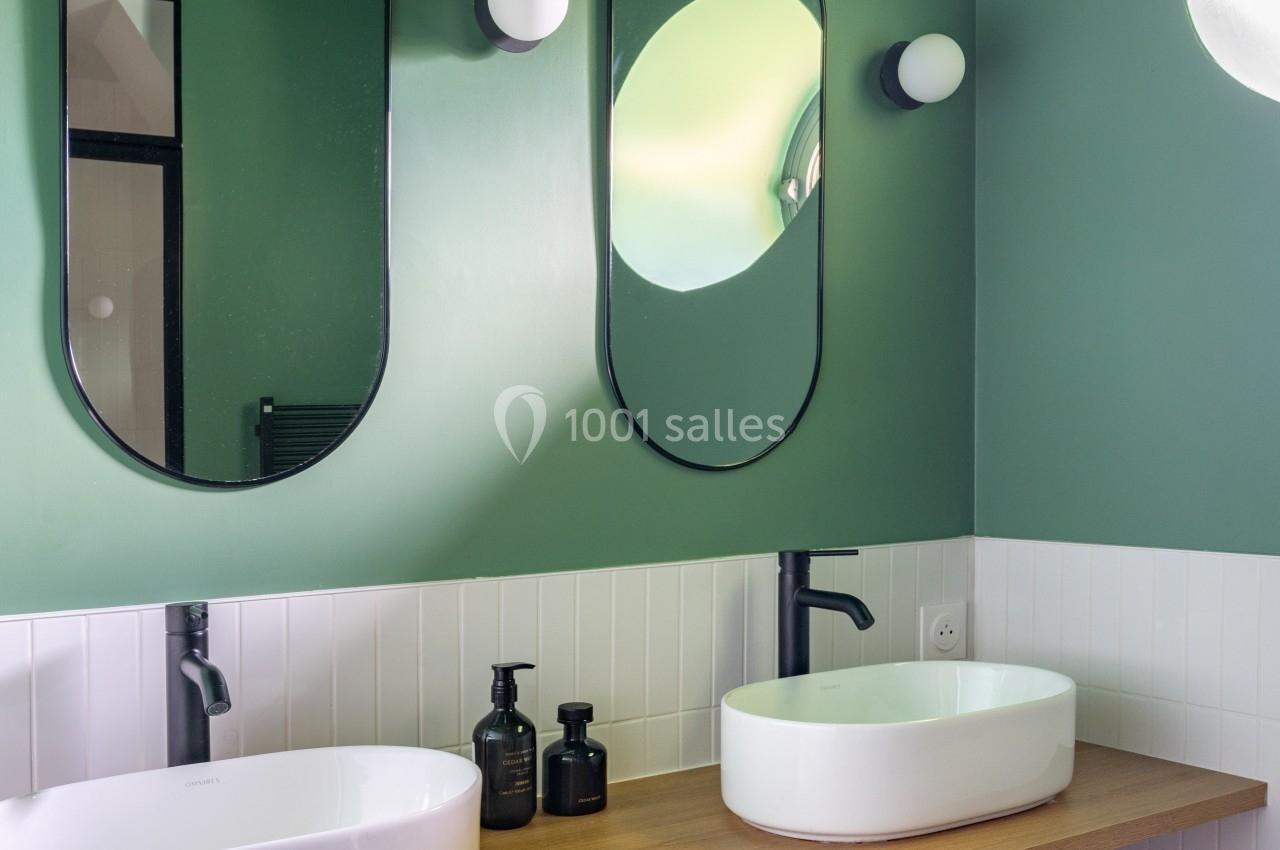 Salle de bain moderne avec murs verts, deux miroirs ovales, vasques blanches et plan de travail en bois.