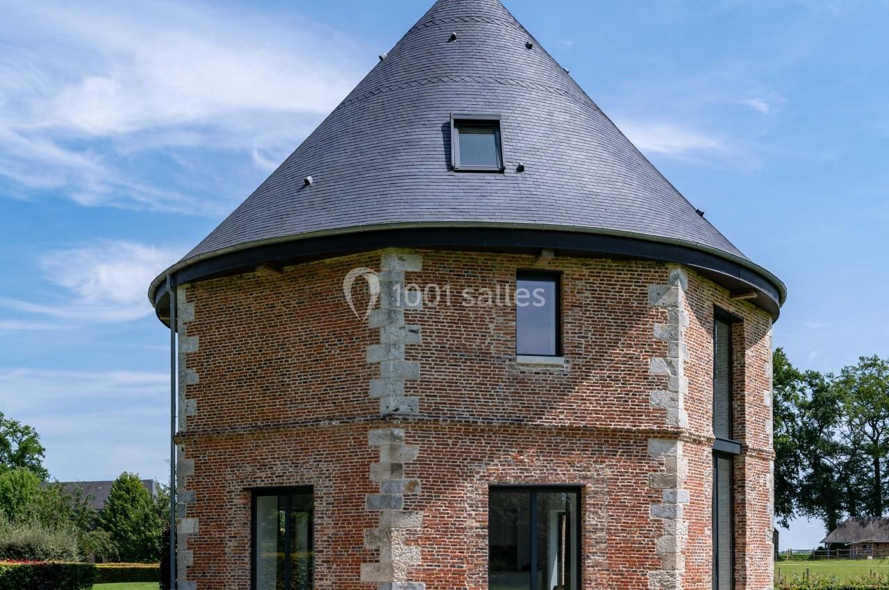 Bâtiment circulaire en briques avec toit en ardoise, entouré de pelouse, table et chaises noires au premier plan.
