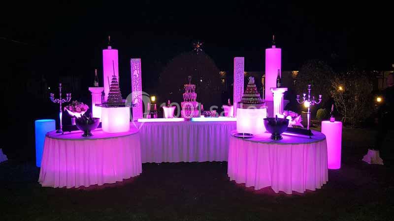 Location salle Argueil (Seine-Maritime) - Domaine de Clairval #23 Table décorative illuminée en rose avec des desserts, chandeliers et colonnes lumineuses dans un cadre nocturne.