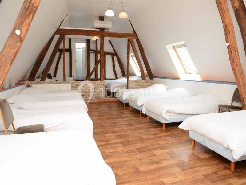 Location salle Argueil (Seine-Maritime) - Domaine de Clairval #28 Dortoir mansardé avec plusieurs lits simples alignés, poutres apparentes et parquet en bois clair.