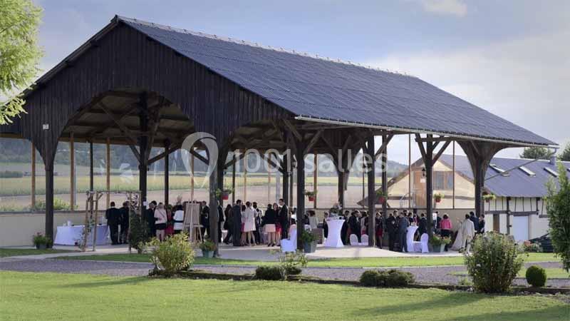 Location salle Argueil (Seine-Maritime) - Domaine de Clairval #20 Structure en bois ouverte accueillant un événement avec des invités debout et des tables dressées, entourée de verdure.