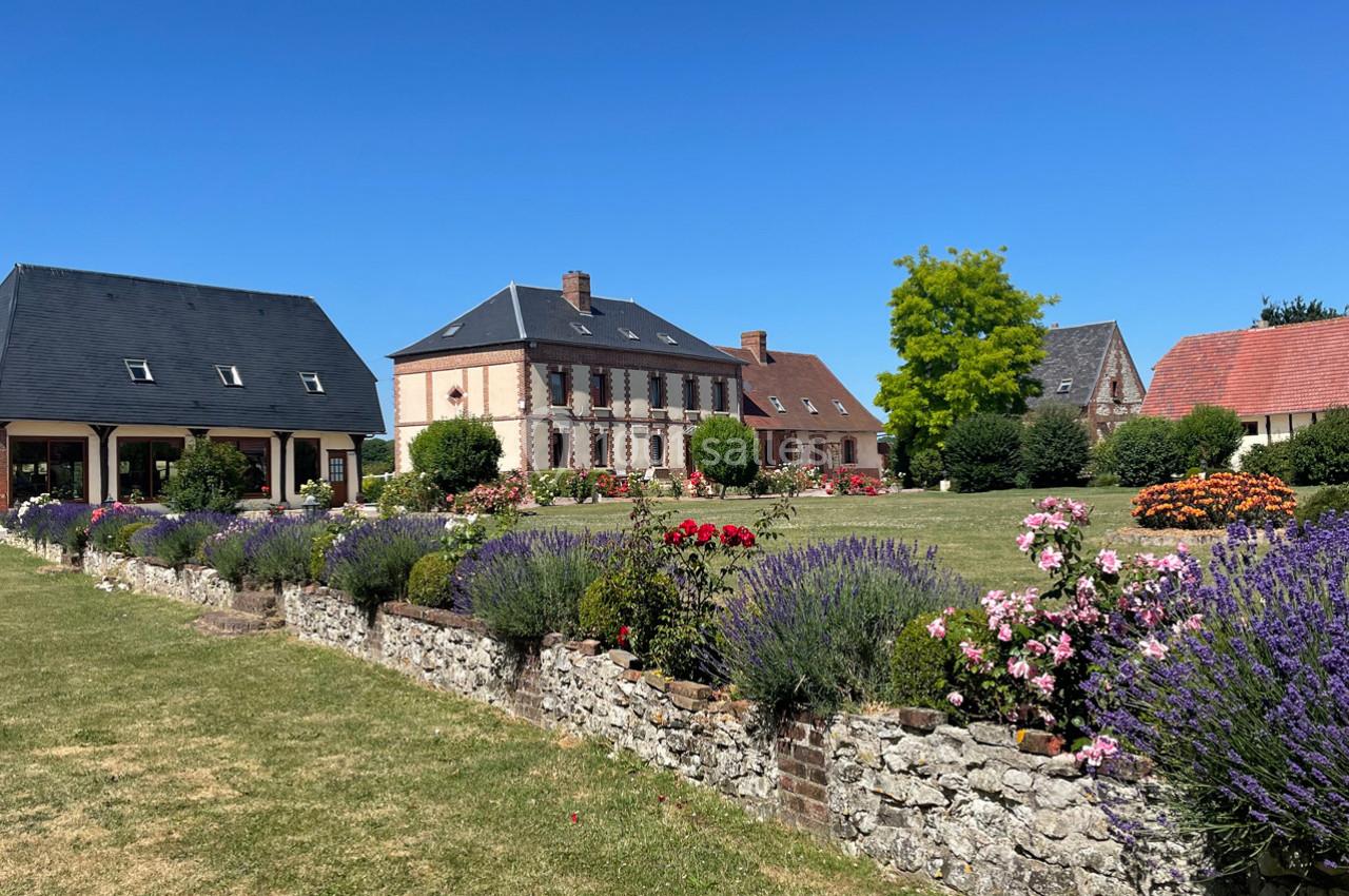 Location salle Argueil (Seine-Maritime) - Domaine de Clairval #3 Jardin fleuri avec lavandes, rosiers et murets en pierre devant des maisons à colombages sous un ciel bleu.