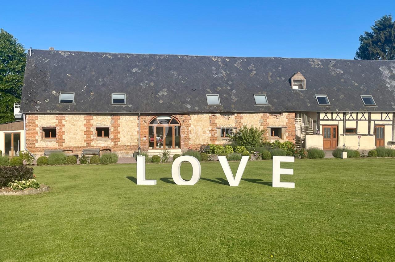 Location salle Argueil (Seine-Maritime) - Domaine de Clairval #6 Grand bâtiment en briques et colombages avec pelouse verte, décoré de grandes lettres blanches formant le mot ’LOVE’.