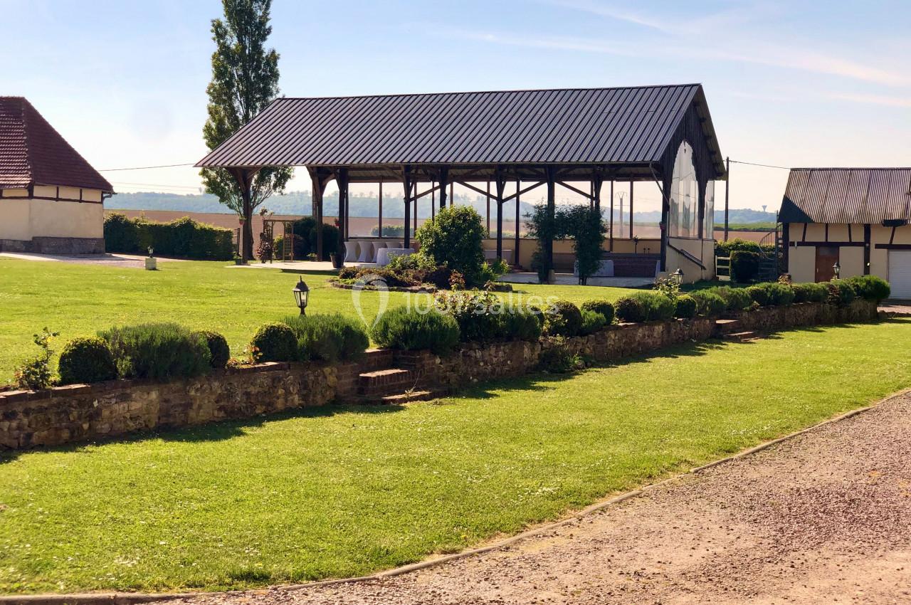 Location salle Argueil (Seine-Maritime) - Domaine de Clairval #7 Abri en bois ouvert entouré de pelouses bien entretenues, avec des bâtiments ruraux en arrière-plan.