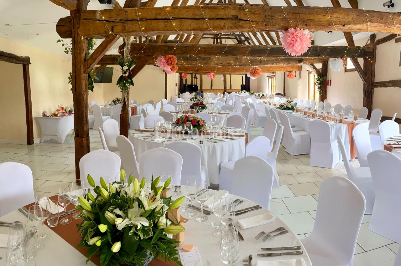 Location salle Argueil (Seine-Maritime) - Domaine de Clairval #10 Salle de réception décorée avec des tables rondes dressées, des fleurs et des poutres apparentes en bois.