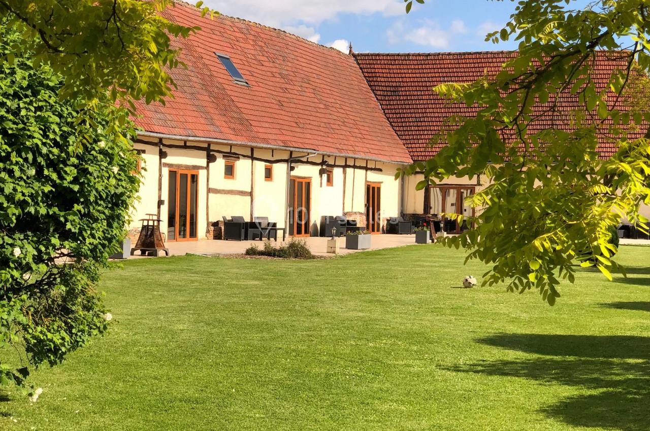Location salle Argueil (Seine-Maritime) - Domaine de Clairval #14 Bâtiment à toit rouge entouré de verdure avec une pelouse bien entretenue sous un ciel partiellement nuageux.