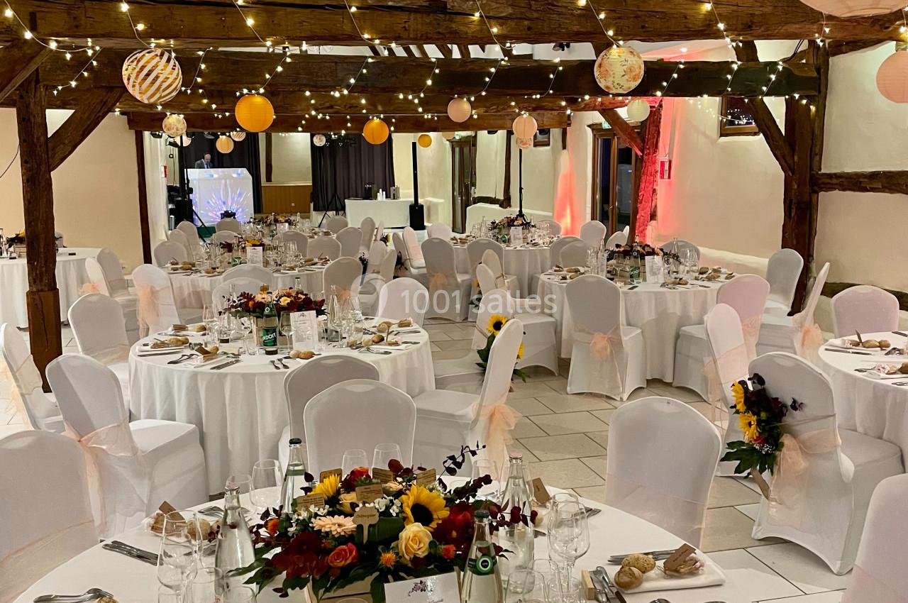 Location salle Argueil (Seine-Maritime) - Domaine de Clairval #19 Salle de réception décorée avec des tables rondes dressées, des guirlandes lumineuses et des fleurs au centre des tables.