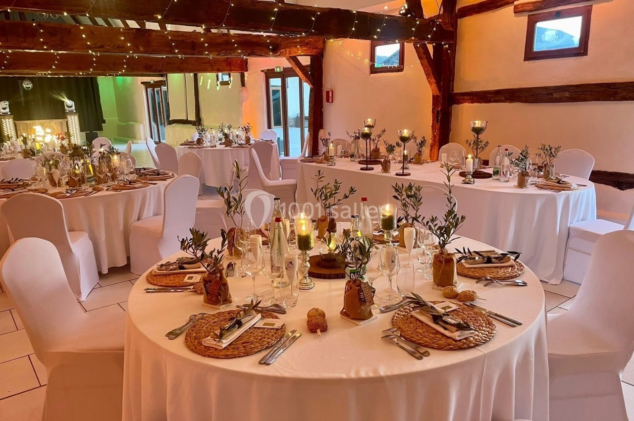 Location salle Argueil (Seine-Maritime) - Domaine de Clairval #1 Salle de réception décorée avec des tables rondes, nappes blanches, bougies et éléments végétaux dans une ambiance…