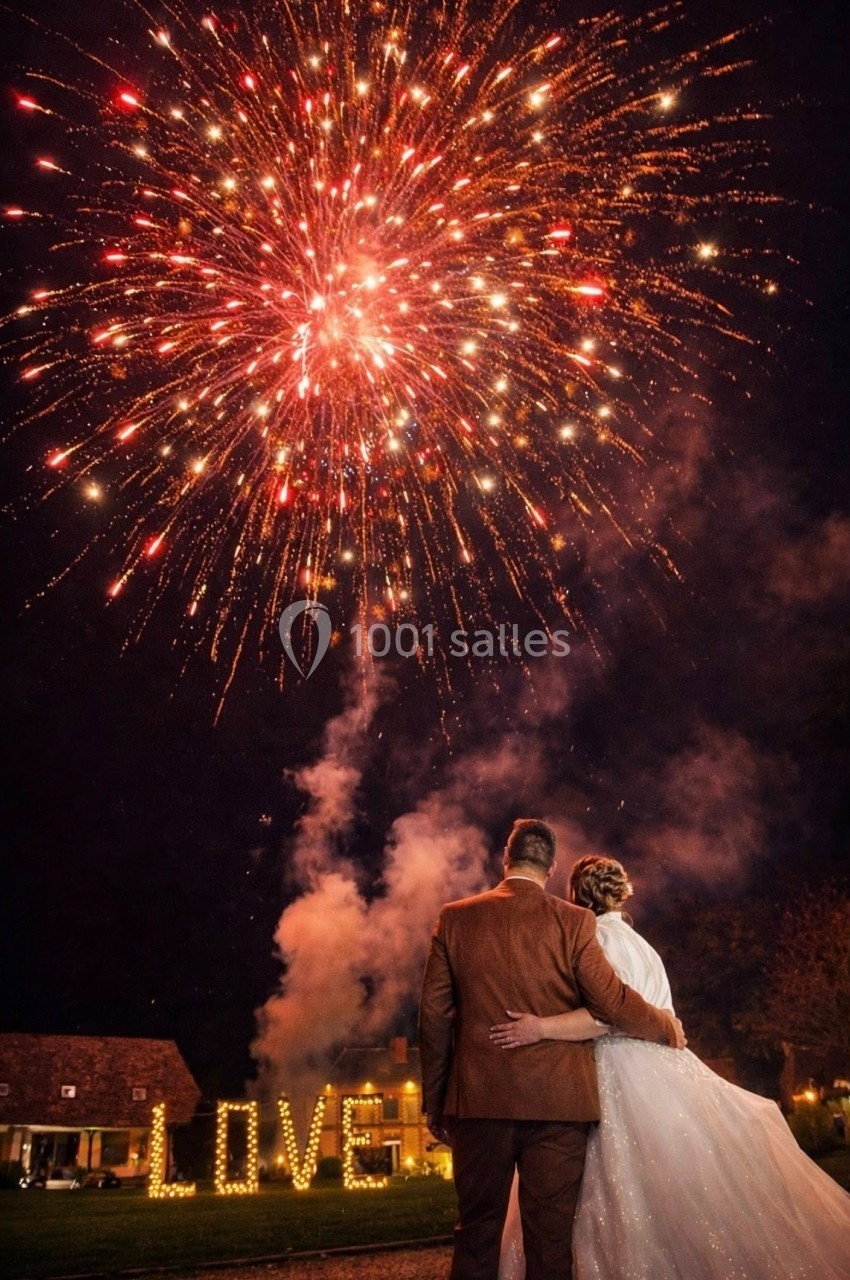 Location salle Argueil (Seine-Maritime) - Domaine de Clairval #3 Un couple observe un feu d'artifice éclatant dans le ciel nocturne, avec le mot ’LOVE’ illuminé en arrière-plan.