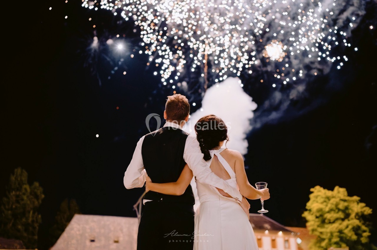 Location salle Argueil (Seine-Maritime) - Domaine de Clairval #4 Un couple de dos observe un feu d'artifice éclatant dans le ciel nocturne, tenant un verre et s'enlaçant.