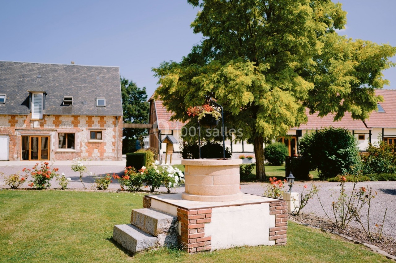 Location salle Argueil (Seine-Maritime) - Domaine de Clairval #7 Puits décoratif en pierre entouré de fleurs, situé dans un jardin avec des bâtiments en arrière-plan.