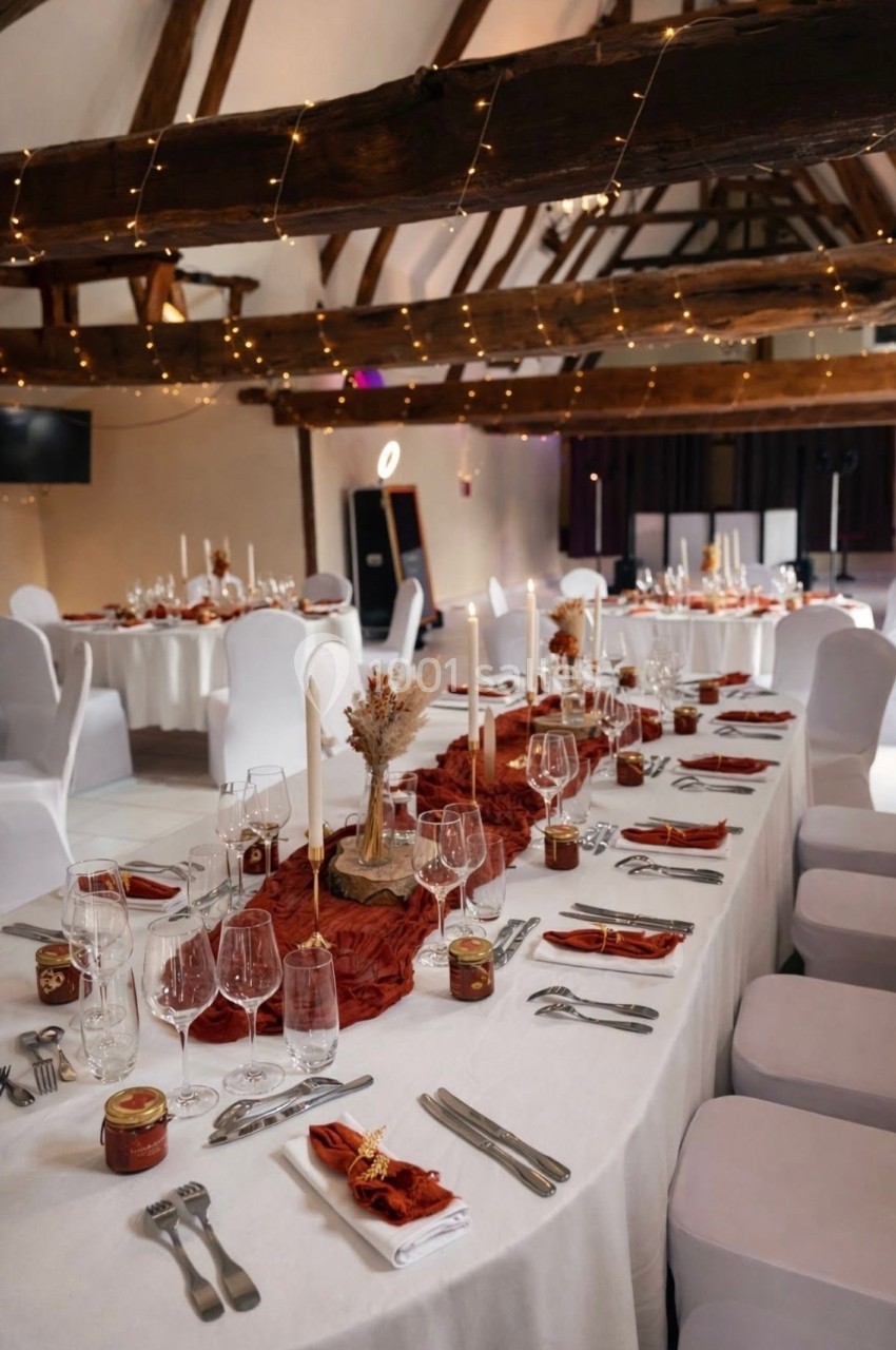 Location salle Argueil (Seine-Maritime) - Domaine de Clairval #9 Salle de réception décorée avec des tables dressées, nappes blanches, bougies et accents rouges sous une charpente en bois.