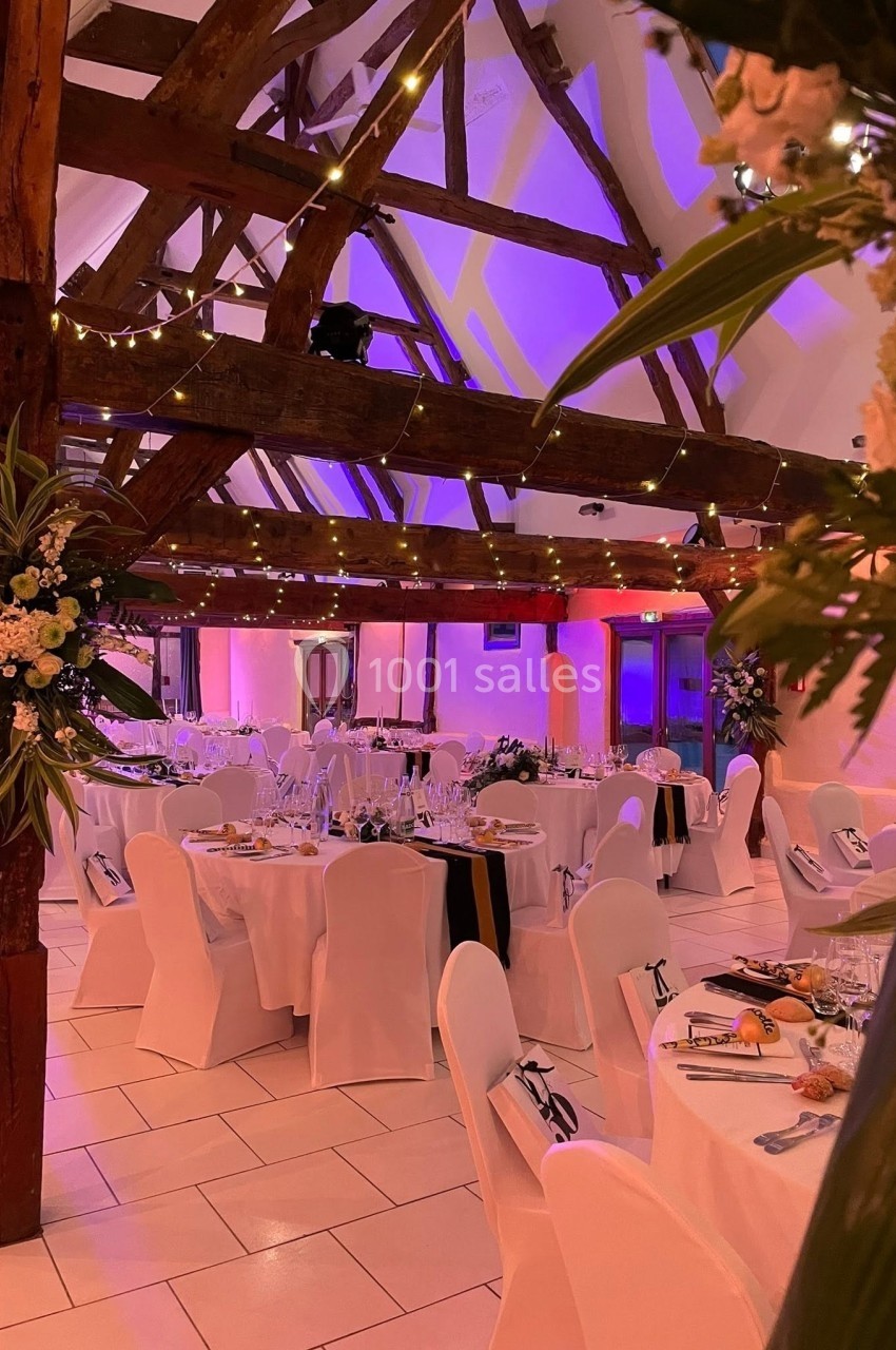 Location salle Argueil (Seine-Maritime) - Domaine de Clairval #10 Salle de réception décorée avec des tables dressées, des chaises blanches et des guirlandes lumineuses sous une charpente en…