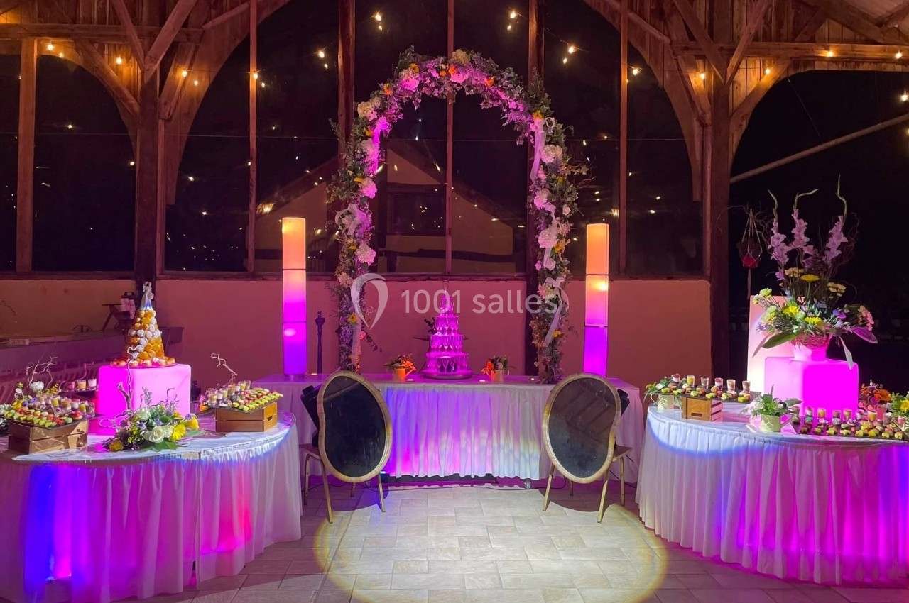 Location salle Argueil (Seine-Maritime) - Domaine de Clairval #13 Salle décorée pour un événement avec arche florale, tables garnies et éclairage rose et chaleureux.