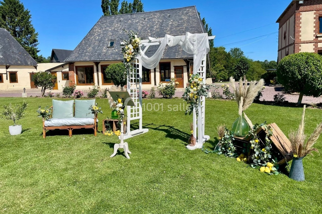 Location salle Argueil (Seine-Maritime) - Domaine de Clairval #14 Décoration de mariage en extérieur avec arche fleurie, banc, et éléments végétaux sur une pelouse devant des bâtiments.