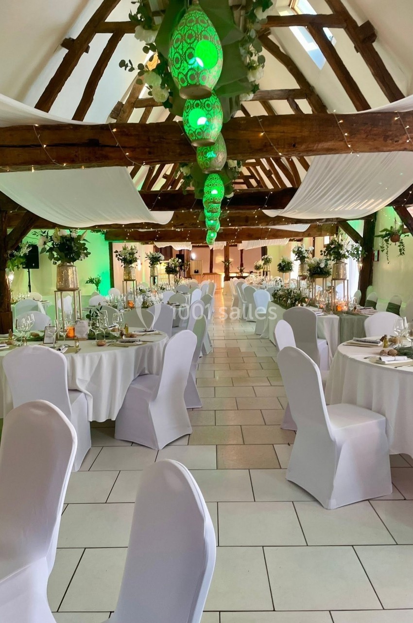 Location salle Argueil (Seine-Maritime) - Domaine de Clairval #16 Salle de réception décorée avec des tables rondes, chaises blanches et lanternes vertes suspendues au plafond en bois.