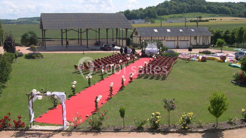 Location salle Argueil (Seine-Maritime) - Domaine de Clairval #21 Allée rouge bordée de chaises et ballons menant à une arche décorée, installée dans un jardin pour une cérémonie.