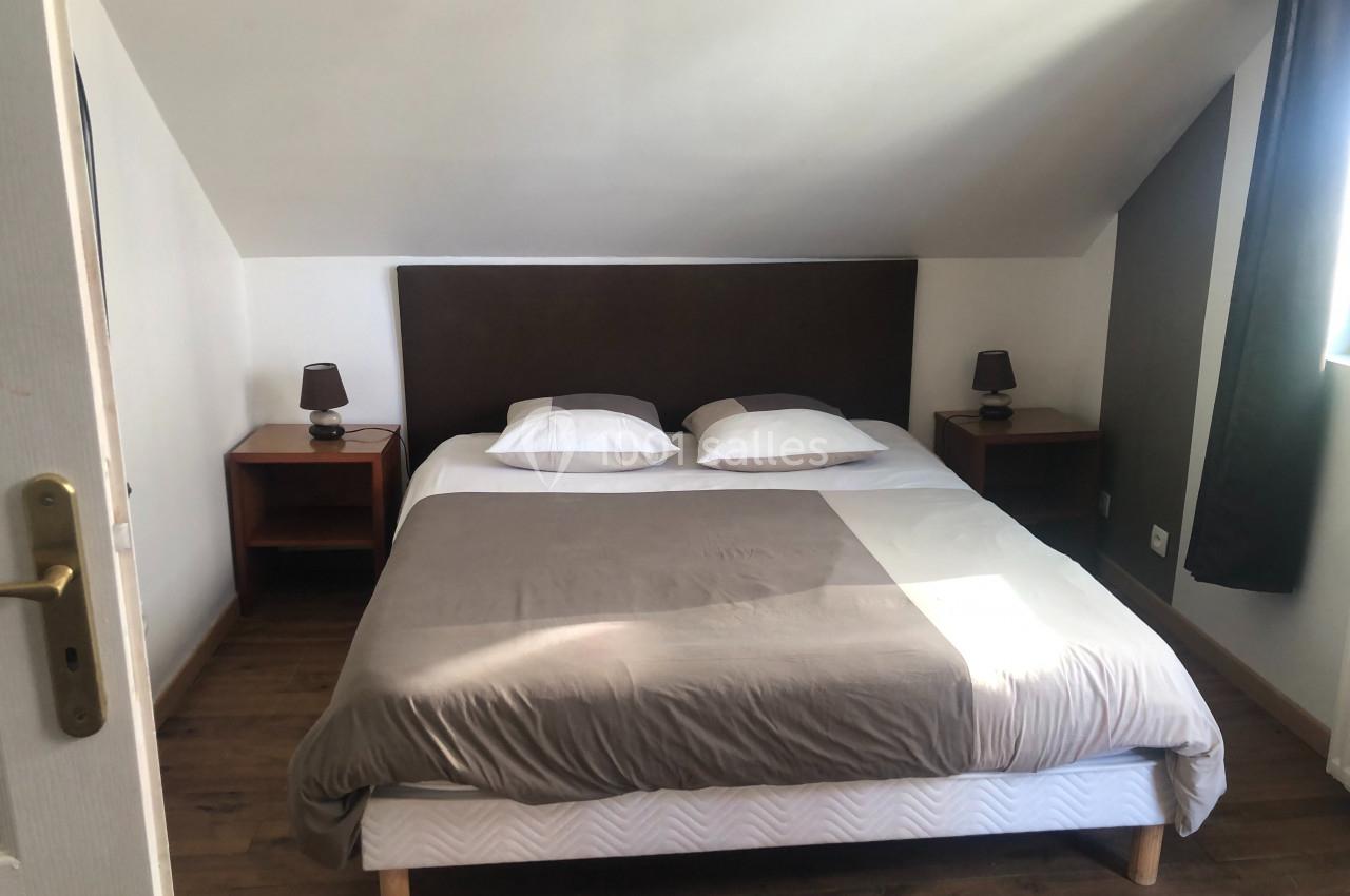 Chambre marron Lit double avec tête de lit sombre, draps gris et blancs, encadré par deux tables de chevet avec lampes, dans une chambre…