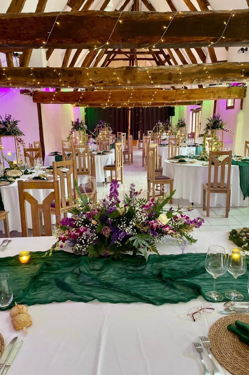 Décoration - Grande Clairval Salle de réception décorée avec des tables rondes, nappes blanches, chemins de table verts et compositions florales.