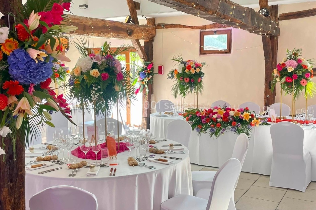 Décoration - Grande Clairval Salle de réception décorée avec des tables rondes, nappes blanches et compositions florales colorées.