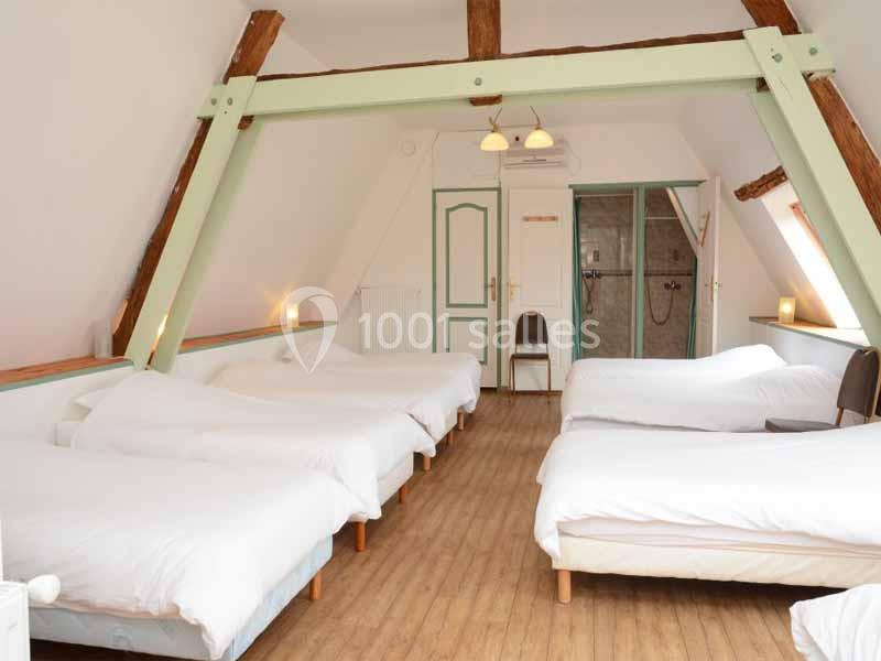 Dortoir Okta - Intérieur Chambre mansardée avec cinq lits simples, poutres apparentes, sol en bois et salle de bain attenante.
