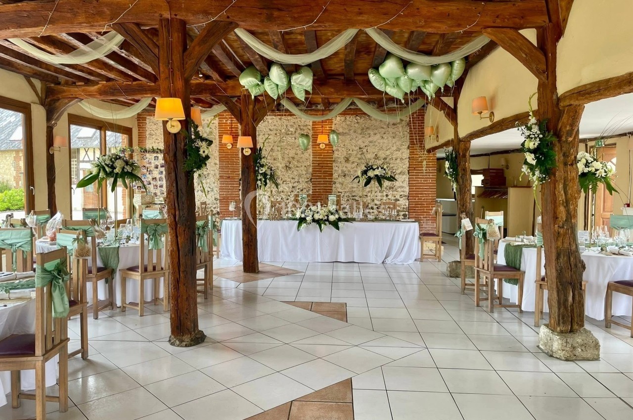 La Charretterie - Intérieur Salle de réception décorée pour un mariage, avec tables dressées, fleurs blanches et vertes, et poutres en bois apparentes.
