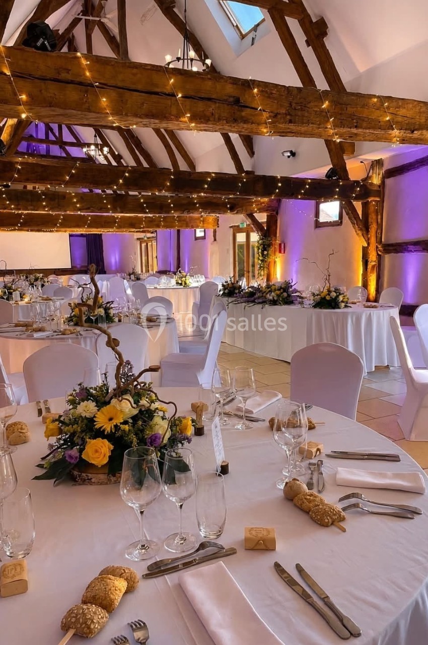 La Grande Clairval - Intérieur Salle de réception décorée avec des tables rondes dressées, des fleurs et des guirlandes lumineuses suspendues.