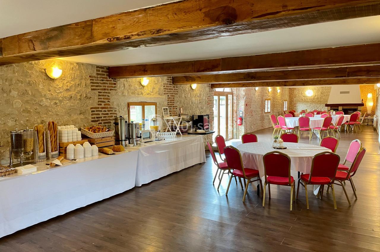 Le Manoir - Intérieur Salle de réception avec tables rondes dressées et buffet installé le long d'un mur en pierre apparente.