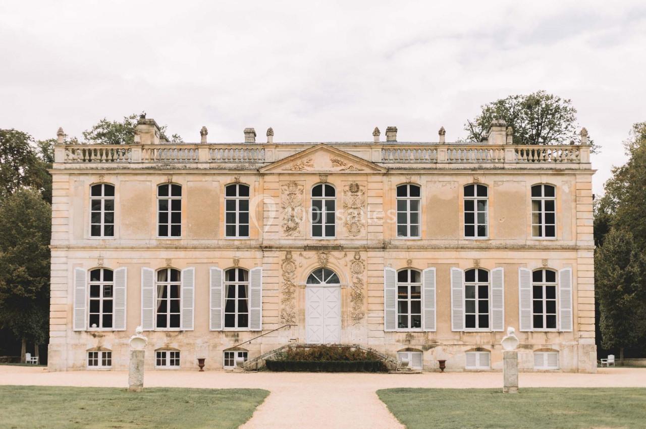 Façade d'un château ancien avec des volets clairs, des fenêtres symétriques et un jardin à l'avant.