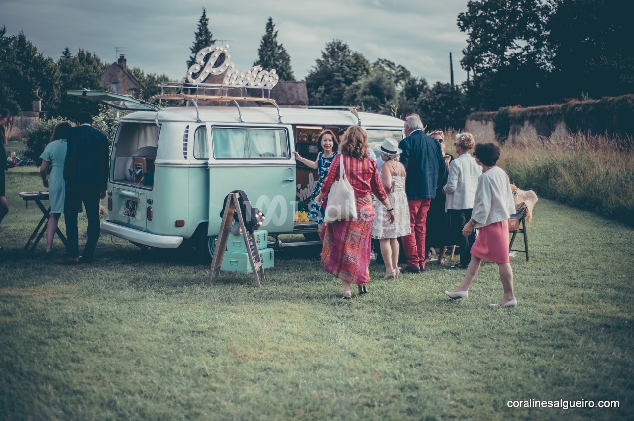 Un groupe de personnes se rassemble autour d'un van vintage aménagé, stationné dans un espace vert.
