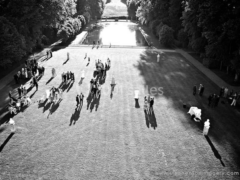 Vue aérienne en noir et blanc d'un jardin avec des groupes de personnes dispersés sur une pelouse près d'un bassin.