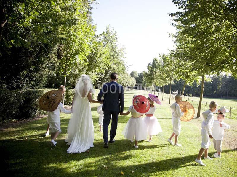 Un couple de mariés marche dans un parc verdoyant, accompagné d'enfants portant des ombrelles colorées.