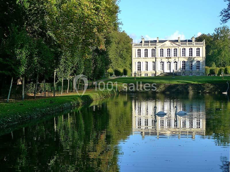 Façade d'un château blanc entouré d'arbres, avec un étang en premier plan reflétant le bâtiment et deux cygnes.
