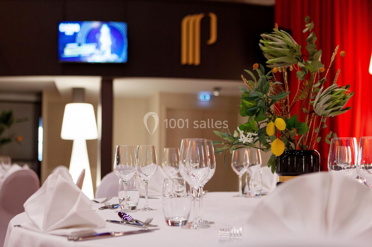 Table dressée avec nappes blanches, verres et serviettes pliées, décorée d'un bouquet floral dans une salle élégante.