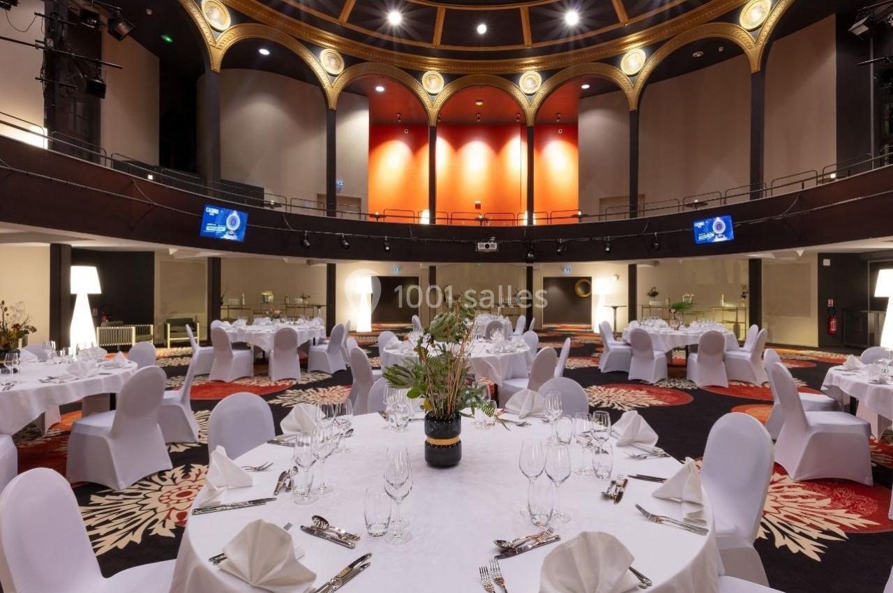 Salle de réception élégante avec tables rondes dressées, nappes blanches et décorations florales, sous un plafond voûté.